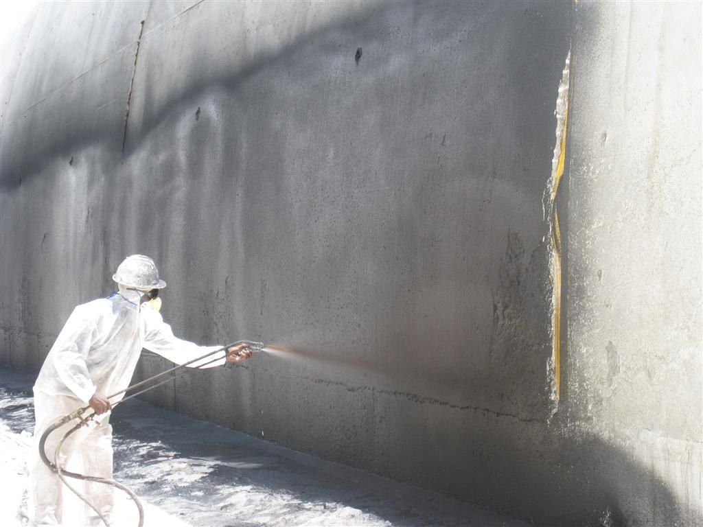 Ouvrier en combinaison projetant un enduit étanche gris sur un mur en béton